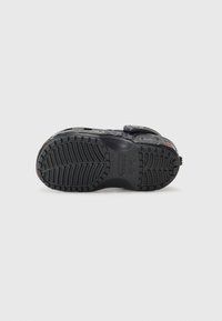 Black rubber shoe sole with a textured tread pattern, featuring circular hardware accents and adjustable fastening mechanism on the side.