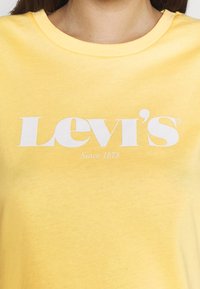 Camiseta de algodón amarilla con un logo blanco de "Levi's" y el texto "Desde 1873". Cuello redondo con una textura suave.