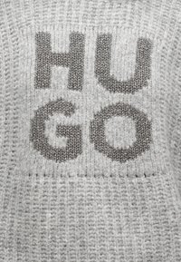 Gray knit sweater featuring large "HUGO" letters in darker gray, with a textured finish and ribbed pattern throughout.