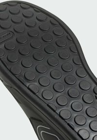 Suola di scarpa in gomma nera con un motivo di  bubbole circolari rialzate, con un bordo testurizzato e una sezione centrale liscia.