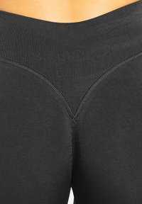 Leggings neri a vita alta con materiale strutturato ed elastico. Presentano un dettaglio di cucitura a forma di V nella parte posteriore della vita e un logo del marchio sottile.