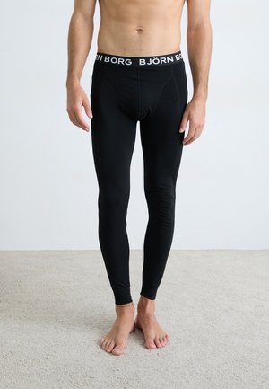 Schwarze dehnbare Leggings mit enger Passform, ausgestattet mit einem weißen Logo-Bund. Glatte Textur und taillierter Schnitt bis zu den Knöcheln.