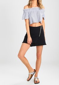 Pruhovaný crop top bez ramínek, černá denimová zavinovací sukně se zipovým detailem a ploché stříbrné sandály.