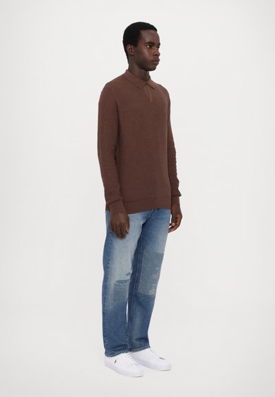 Brun langærmet polo skjorte med krave, parret med lyseblå slidte denimjeans og hvide sneakers. Simpelt design med ribbede manchetter.