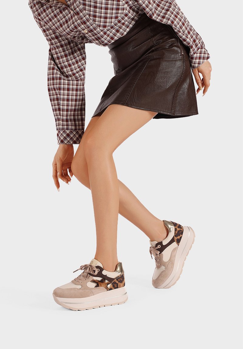 Zapatillas beige con una suela gruesa, acentos de ante y estampado animal, detalles en dorado y cordones en la parte delantera, combinadas con una falda de cuero.