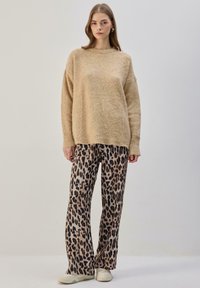 Beežikas pehme kampsun lõdvaistmelise lõikega, kombineeritud tan-nahavärvi ja musta leopardimustriliste laia säärega pükstega ning helevärviliste tossudega.