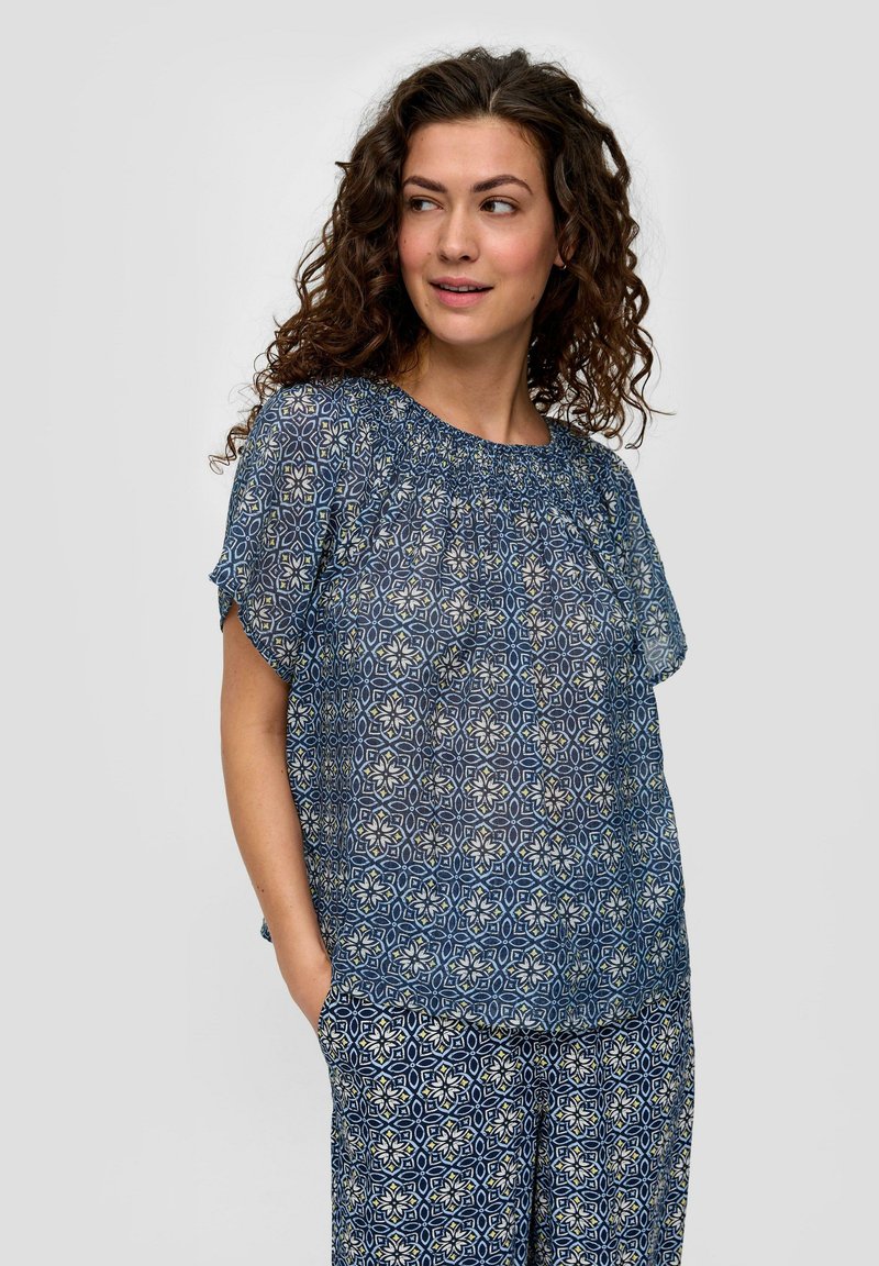 Blauw gemarmerde blouse met korte mouwen en gathers bij de hals. De stof is lichtgewicht en heeft geometrische bloemenpatronen in crème en blauw.