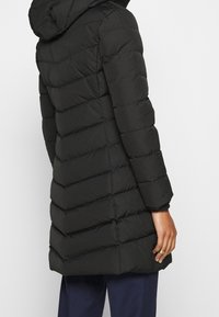 Černá péřová bunda s kapucí, se sv quiltovanými částmi, dlouhými rukávy a mírně zúženým designem v pase.