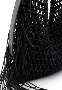 Sac à main noir crocheté avec de longs détails en cuir frangé et une bandoulière en cuir lisse sur fond blanc.
