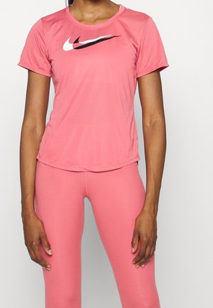 Personne portant un haut à manches courtes rose et des leggings assortis, le haut présente des motifs swoosh blancs et noirs superposés sur la poitrine.