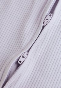 Gros plan de deux curseurs de fermeture éclair blancs adjacents sur un tissu côtelé, partiellement zippés, montrant la texture détaillée et les coutures.