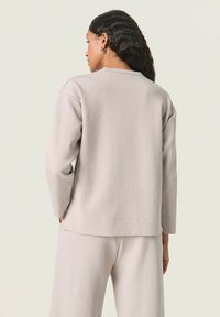 Lys grå sweatshirt med lange ærmer, cropped design og rund halsudskæring. Glat tekstur, minimale syningsdetaljer og afslappet pasform.