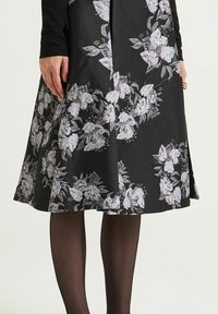 Jupe noire à motif floral avec une coupe évasée, ornée de fleurs blanches et roses. Le tissu présente une finition texturée, agrémentée d'une fente latérale discrète.