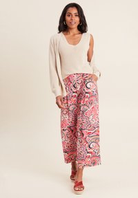 Top in maglia beige abbinato a pantaloni a gamba larga rosa con motivo floreale e sandali platform rossi. Presenta una texture morbida e un design vivace.