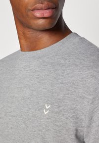 Grauer Baumwollpullover mit ribbeligem Rundhalsausschnitt und kleinem weißen Logo auf der Brust. Glatte Textur und normale Passform.