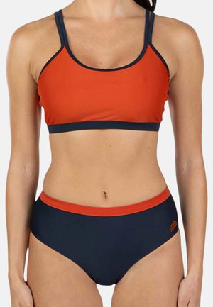 Donna che indossa un costume da bagno due pezzi con top arancione e parte inferiore blu navy con fascia arancione in vita.