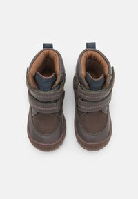 Chaussures montantes marron en textile et cuir, dotées de deux bandes Velcro, d'une cheville rembourrée et d'une semelle en caoutchouc texturé.