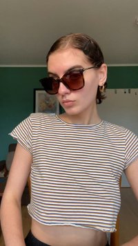 Brązowa paskowana bluzka o krótkim rękawie w stylu crop top, zestawiona z oversized, ciemnobrązowymi okularami przeciwsłonecznymi. Okulary mają grubą oprawę i duże soczewki.