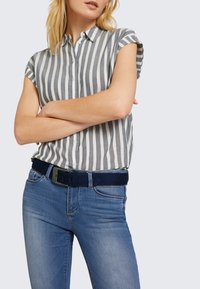 Šedá a biela pruhovaná košeľa s krátkymi rukávmi a gombíkovou légou, skombinovaná s modrými džínsami a tmavomodrým opaskom so štvorcovou prackou.