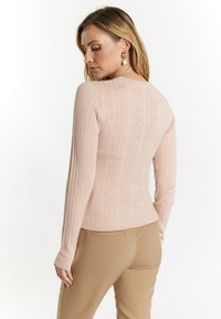 Hellrosa gerippter Pullover mit Rundhalsausschnitt und langen Ärmeln, der ein strukturiertes Muster aufweist. Kombiniert mit beigen, maßgeschneiderten Hosen.