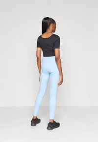 Μαύρο κοντό τοπ και ανοιχτό μπλε κολάν. Απαλή ύφανση, εφαρμοστό σχέδιο, ψηλόμεσο κολάν, συνδυασμένο με μαύρα αθλητικά παπούτσια.