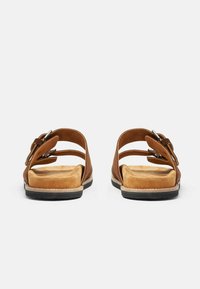 Smeđe kožne sandale s dva podesiva remena, mekanom bež uloškom i teksturiranom crnom gumom potplatom. Imaju ukrasni detalj u obliku mašne.