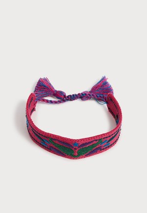Bracelet en tissu tissé rouge, violet, vert et bleu avec un motif papillon symétrique et des liens à pampilles tressés sur fond blanc.