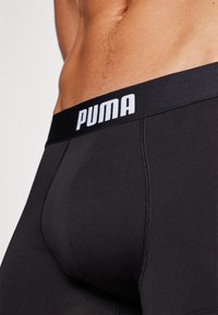 Black Puma boxer briefs with a thick waistband featuring white logo text. The fabric is smooth, stretchy, and fitted with reinforced stitching.