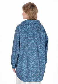 Blå leopardmönstrad jacka med huva, med långa ärmar och en avslappnad passform. Materialet verkar mjukt med ett livfullt mönster.