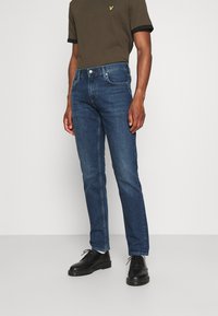 Vaqueros de mezclilla azul oscuro con corte recto, que presentan un diseño de cinco bolsillos y detalles de costura sutiles. Combina con una camiseta verde oscura.