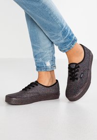 Svarta glittriga sneakers med platta sulor, runda tår och svarta snören. Jeansen är i en urtvättad blå färg med lätt slitage.