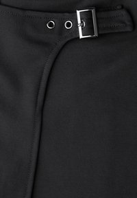 Tela negra con textura suave que presenta un cinturón, hebilla de metal y ojales, creando un detalle de diseño asimétrico.