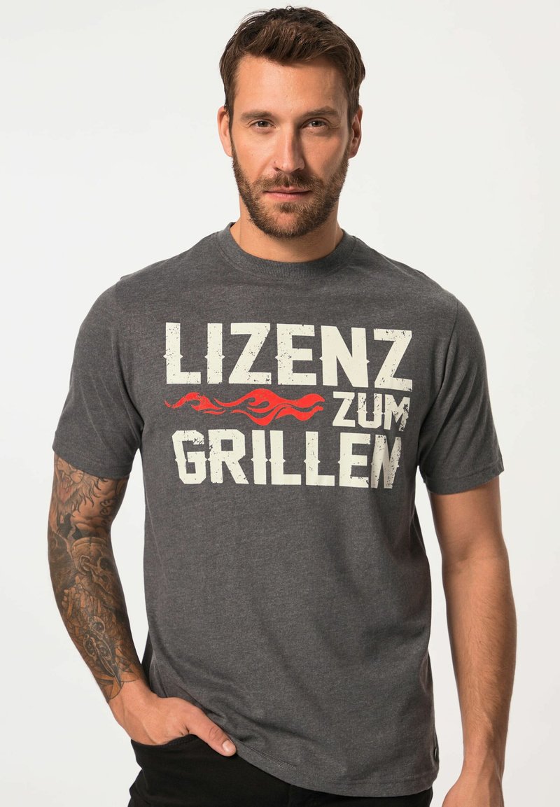 Šedé bavlněné tričko s krátkým rukávem, které zaujme výrazným bílým a červeným textem "LIZENZ ZUM GRILLEN" a je doplněno grafikou plamene.