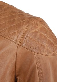 Tan leren jas met een schouder met een gewatteerde textuur, zichtbare stiksels, een gladde afwerking en een afgeronde vorm. Accentuerende naden versterken het ontwerpdetail.