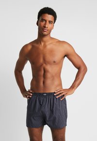 Heren boxershorts in donker marineblauw, met verticale witte strepen, een elastische tailleband en een enkele knop aan de voorkant voor sluiting.