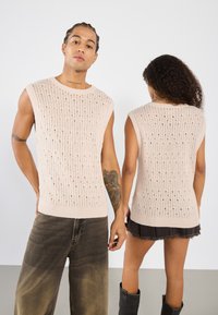 Haut sans manches en tricot beige avec un motif texturé et des mailles ouvertes. Doté d'un col rond et d'un ourlet côtelé. Coupe décontractée.