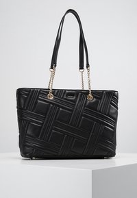 Czarna skórzana torba tote z plecionym wzorem, złotymi łańcuszkami oraz zrównoważoną formą. Solidna podstawa z metalowymi stopkami.