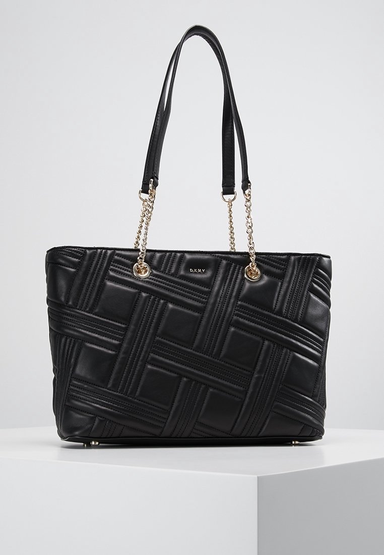 Czarna skórzana torba tote z plecionym wzorem, złotymi łańcuszkami oraz zrównoważoną formą. Solidna podstawa z metalowymi stopkami.