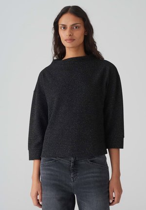 Zwarte textuur top met een boxy silhouet, driekwart mouwen en een brede halslijn. Gemaakt met donkergrijze jeans. Subtiele metallic accenten.