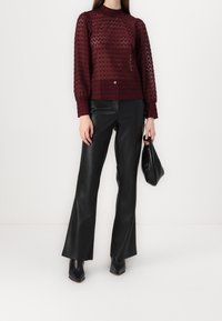 Burgundy strikket sweater med lange ærmer, parret med sorte læder flared bukser og sorte stiletto ankelstøvler, samtidig med at der holdes en lille taske.