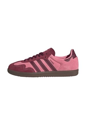 Niskie trampki Adidas Samba z różowego i bordowego zamszu z ciemnobrązową podeszwą i trzema paskami marki po bokach.