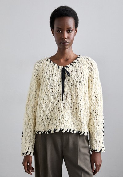 Creme strikket sweater med et tekstureret mønster, der har en rund halsudskæring, sorte detaljer og en båndlukning. Afslappet, cropped pasform.