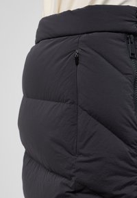 Zwarte pufferrok met een doorgestikt ontwerp, ritszak en een elastische tailleband. Het materiaal heeft een gladde, matte textuur.