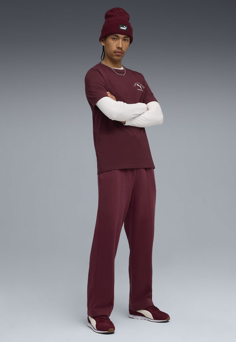 Bordeaux atletisk sæt med en kortærmet t-shirt over en langærmet hvid top, matchende bordeaux bukser og bordeaux sneakers.