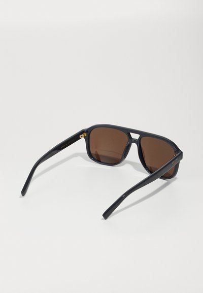 Gafas de sol rectangulares negras con lentes marrones oscuros. Están hechas de un material brillante y presentan detalles en dorado en las patillas.