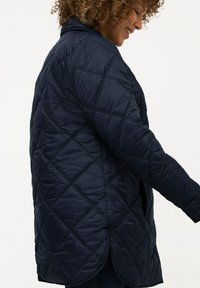 Námořnická prošívaná bunda s diamantovým vzorem, vyrobená z hladké látky. Má kulatý lem a dlouhé rukávy s manžetami.