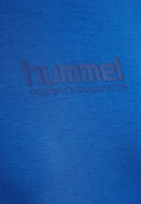 Blauses Sporthemd mit glatter Textur. Verfügt über das geprägt "hummel PERFORMANCE" Logo in einem dunkleren Farbton, das die Markenidentität betont.