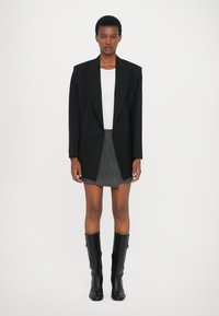 Svart oversized blazer, hvit tettsittende topp, grå mini-skjørt og svarte knestøtte støvler; glatt stoff, strukturert design og skreddersydde detaljer.