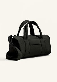 Svart vadderad duffelväska med två övre handtag och en avtagbar axelrem, med en platt framficka och mjuk textur.
