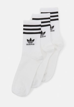 Calcetas deportivas blancas con tres rayas negras en la parte superior y un logo de Adidas en negro en el lateral. Textura suavemente tejida.